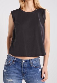 Top corto sin mangas de color gris oscuro, hecho de suave tela de algodón, con un cuello redondo y un dobladillo limpio. Combinado con jeans azules desgastados.