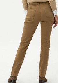 Pantalones ajustados marrones con una textura suave, dos bolsillos traseros y un diseño de pierna recta, combinados con tacones marrones.