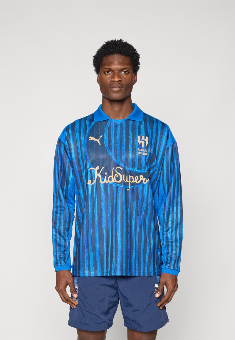 Maglietta da calcio a maniche lunghe blu con righe verticali, dotata di un design con colletto, logo dorato e dettagli, abbinata a pantaloni corti blu navy.