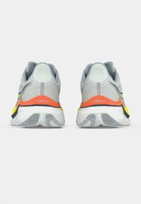 Svijetlosivi trkački tenisice s teksturiranim gornjim dijelom, ukrašene narančastim i žutim naglascima, istaknutom amortizacijom na peti i dizajnom gumene potplate.