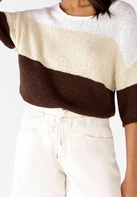 Jersey de punto con rayas horizontales en blanco, crema y marrón, con cuello redondo y mangas cortas. Combinado con pantalones blancos.