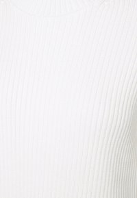 Rippstrick weißer Pullover mit hohem Kragen, der vertikale Linien, eine weiche Textur und eine figurnahe Passform aufweist.