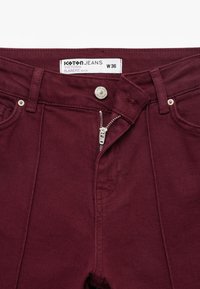 Burgundy denim jeans med flare-fit, der har en sølvfarvet lynlås, knaplukning og forlommer. Mærket siger "Koton Jeans W 36."