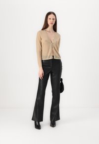 Beige, tætsiddende cardigan med V-hals og knaplukning, parret med højtaljede, sorte læderbukser med flared ben. Glatte teksturer, minimalistisk design.