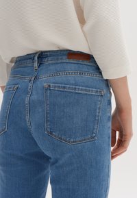 Lichtblauwe spijkerbroek met een aansluitend ontwerp, voorzien van twee achterzakken en een bruine leren label op de tailleband.