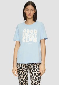 Lichtblauwe T-shirt met korte mouwen met vetgedrukte witte tekst "GOOD ENERGY CLUB." Gecombineerd met leggings met een panterprint.