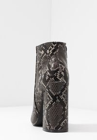 Stivaletto da donna con tacco alto a blocco e texture serpentina nero e grigio, mostrato da dietro.
