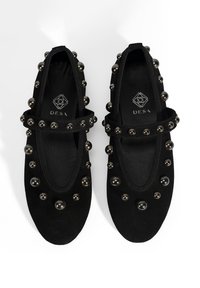 Schwarze Wildleder-Ballerinas mit runder Zehenform, verziert mit metallischen Nieten und einem dekorativen Riemen über dem Spann. Glatte Innenausstattung.