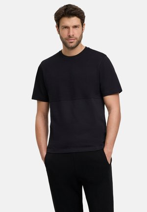 Schwarzes T-Shirt mit kurzen Ärmeln und strukturiertem Mittelteil, Rundhalsausschnitt und geradem Schnitt, kombiniert mit schwarzen Hosen. Minimalistisches Design.