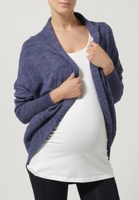 Navy blue knitted cardigan with long sleeves, open front, and ribbed cuffs, worn over a white top, highlighting a round belly shape.