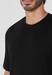 Černé tričko s krátkým rukávem a kulatým výstřihem, hladká bavlněná tkanina a volný střih, který ukazuje minimalistický design.