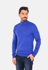 Maglione a collo alto blu in tessuto a maglia, con maniche lunghe, polsini a coste e orlo a coste. Indossato con jeans in denim scuro.