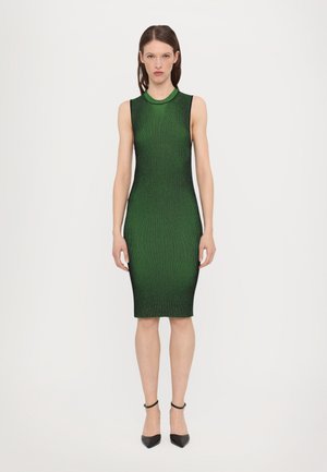 Sleeveless, form-fitting green knit dress with a ribbed texture. Features a high neckline and falls to the knee. Black pointed heels visible.