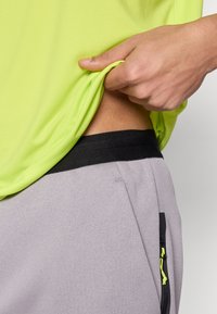 Φωτεινό πράσινο αθλητικό πουκάμισο με ομαλή υφή, σε συνδυασμό με γκρι παντελόνια που φέρουν μαύρη μέση και τσέπη με φερμουάρ με νέον κίτρινες λεπτομέρειες.