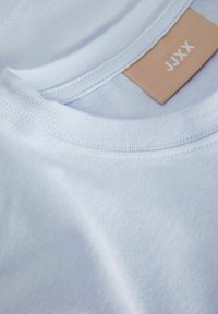 Camiseta de algodón azul claro con cuello redondo de canalé y costuras cosidas. Presenta una etiqueta beige con el texto "JJXX".