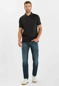 Zwart polo-shirt met een kraag, witte bies en een klein logo op de borst, gecombineerd met blauwe jeans en witte sneakers.