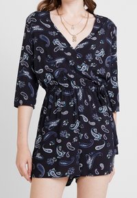 Svart jumpsuit med paisley- och blommönster, 3/4-ärmar, elastisk midja och en lös passform. Tyget verkar lätt och mjukt.