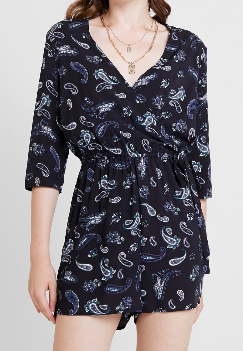 Svart jumpsuit med paisley- och blommönster, 3/4-ärmar, elastisk midja och en lös passform. Tyget verkar lätt och mjukt.