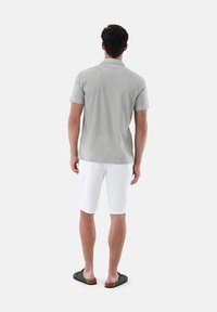 Hellgraues Kurzarm-Polo mit einem dezenten strukturierten Muster, kombiniert mit weißen Shorts und dunklen Sandalen, von hinten betrachtet.