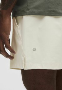Herre træningsshorts i lysecreme med en glat tekstur og sideåbninger. Har et lille sølvlogo på nederste venstre side.