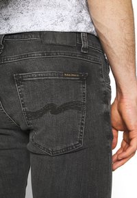 Svarta jeans i denim med klassisk fickdesign och subtilt vågigt sömnadsmönster. Guldfärgad logotyp på bakfickan.