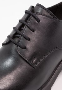 Svart läderskor med stängd snörning, fin sömnad och slätt polerat finish på vit bakgrund.