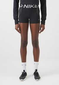 Mustat urheilushortsit, joissa on leveä vyötärönauha hopeisella "NIKE"-logolla ja pistekuvioisilla yksityiskohdilla. Kangas näyttää sileältä ja istuvalta.