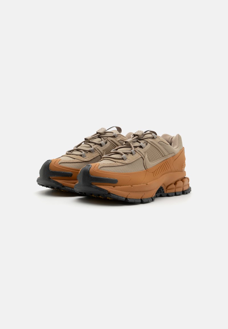 Sportieve sneakers met een beige textielen bovenkant, bruine rubberen accenten, een dikke zwarte zool en decoratieve veters. Q