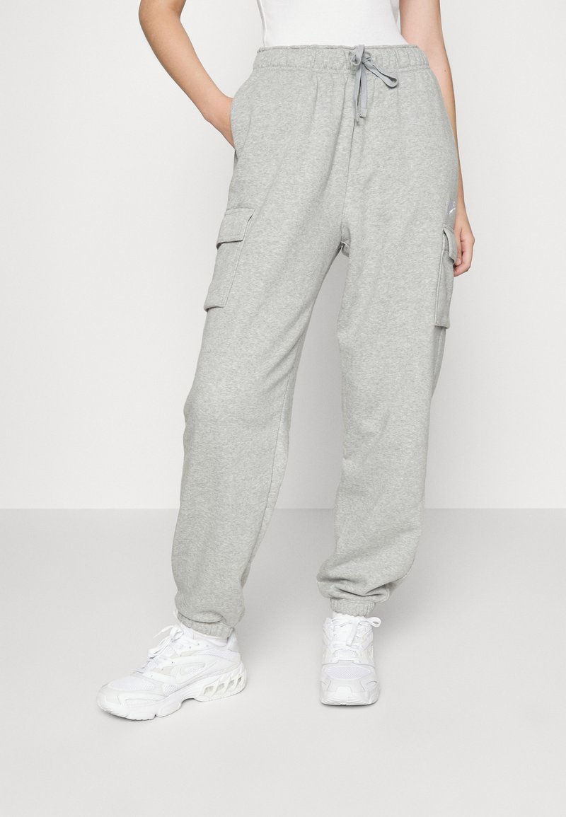 Pantaloni jogging grigi in cotone con fascia elastica in vita, due tasche laterali e polsini elasticizzati, abbinati a scarpe da ginnastica bianche.