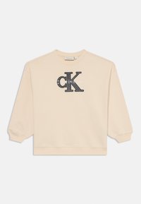 Sudadera beige con cuello redondo y mangas largas. Presenta un logo bordado en negro de "CK" y el texto "calvin klein" en la parte delantera.