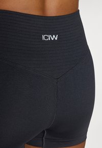 Mustat urheilushortsit, joissa on ribbausvyötärö, tiukka leikkaus ja valkoinen brodeerattu "ICIW" -logo vyötäröllä.