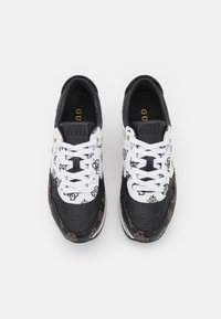 Valkoiset ja mustat tennarit logokuvioilla, tekstiilistä valmistettu päällinen ja tasaiset nauhat. Varustettu kultaisilla yksityiskohdilla sekä sileällä, teksturoidulla pinnalla.