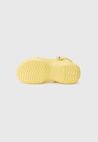 Sabot jaune à enfiler avec semelle texturée et bride ajustable ornée d'un bouton rond argenté, vu de dessous sur un fond clair.