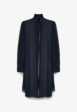 Donkerblauwe blouse met lange mouwen, hoge hals, striklinten aan de voorkant, geplooide mouwen en knoopdetails bij de halslijn.