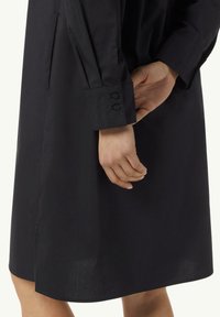 Zwart shirtjurk van gladde stof, met lange mouwen, knopenmanchetten en een zijsplit voor vrijere beweging.