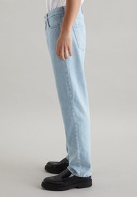 Jeans in denim blu chiaro con vestibilità dritta, dotati di chiusura a bottone, tasche laterali e posteriori, indossati con mocassini neri.