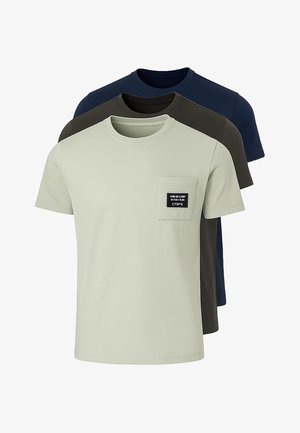 Tres camisetas de manga corta: una verde claro con un bolsillo en el pecho y una etiqueta negra, una marrón oscuro y una azul marino, todas de suave tela de algodón.