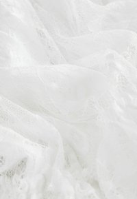 Tissu en dentelle blanche avec des motifs floraux et hexagonaux complexes, texture douce, plis superposés et apparence délicate et transparente.