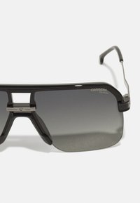 Occhiali da sole polarizzati con una struttura nera in plastica elegante e lenti grigie sfumate. Presentano un ponte in metallo e un design minimalista.
