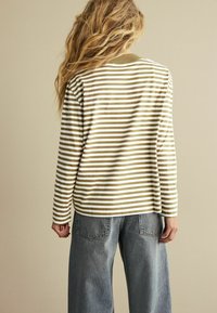 Raidallisia pitkähihaisia pusero vaaleanbeigeissä ja oliivinvihreissä sävyissä, pyöreä pääntie ja rento leikkaus. Yhdistetty korkeavyötäröisiin, leveälahkeisiin farkkuihin.