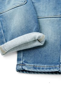 Rukáv džínové bundy s ohrnutým manžetou, světle modré barvy, s vybledlou texturou, kontrastním prošíváním a hladkým povrchem.