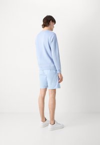 Felpa azzurra e pantaloni sportivi abbinati. La felpa ha un collo rotondo; i pantaloni sono sopra il ginocchio e sono realizzati in tessuto leggero. Sneakers bianche.