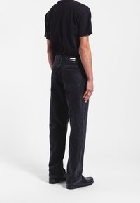Jeans de mezclilla negra con corte recto, con bolsillos traseros, una etiqueta con "DRDENIM" y un ajuste relajado. Llevados con una camiseta negra.