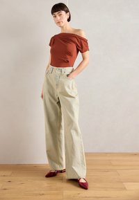 Rust-colored off-shoulder top, relaxed-fit light blue denim wide-leg jeans with front pockets, and red pointed-toe heels.