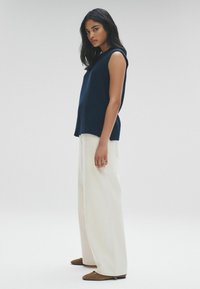 Top smanicato blu navy con tessuto testurizzato, abbinato a pantaloni bianchi a gamba larga e ballerine marroni. Design semplice con una silhouette moderna.