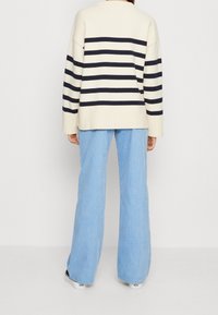 Gestreifter Creme- und Marinepullover mit lockerer Passform, gerippter Struktur; kombiniert mit weit geschnittenen Hosen aus hellblauem Cordstoff und schwarzen Schuhen.