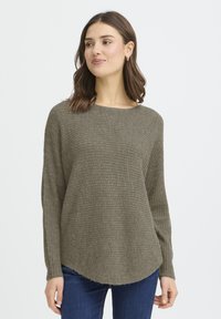 Pull en tricot vert olive à encolure ronde, manches longues, motif texturé et ourlet incurvé, associé à un jean bleu.