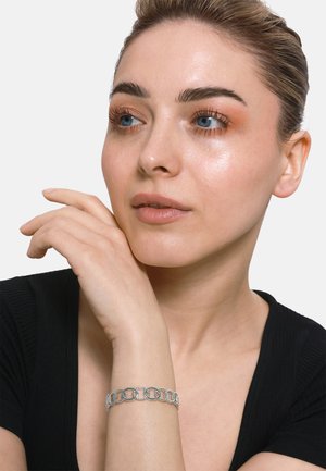 Bracciale in argento con segmenti circolari e testurizzati, indossato su un braccio di pelle chiara. Lo sfondo è bianco semplice e il modello ha un trucco sobrio.
