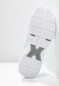 White athletic shoe outsole with a textured surface, featuring ridges and openings for grip, and a gray accent in the center.