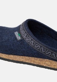 Primo piano di un ciabattino in feltro blu navy con bordino decorato, suola in sughero, fondo in gomma nera e etichetta del marchio Stegmann.